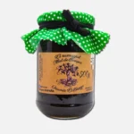 Tarro de mermelada artesanal con tapa de tela verde con puntos blancos, etiquetado con el nombre del producto y detalles de la marca. Ideal para untar en tostadas o como complemento en postres.