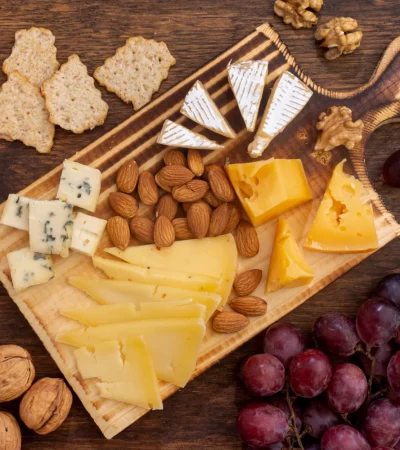 Tabla de quesos variados con almendras, nueces, uvas moradas y galletas sobre una superficie de madera. Ideal para una cena o evento social.
